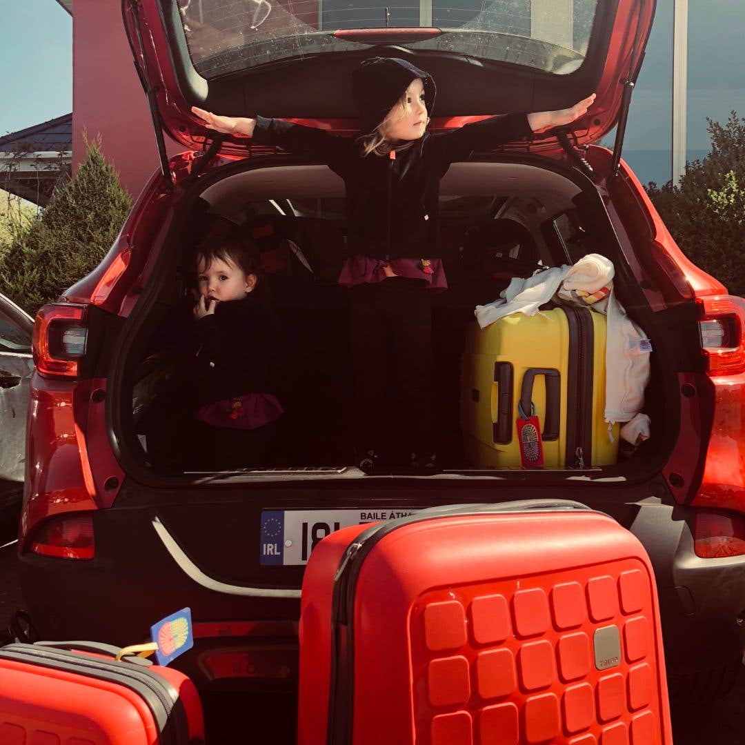 Two little girls in the boot of a car with luggage around them.