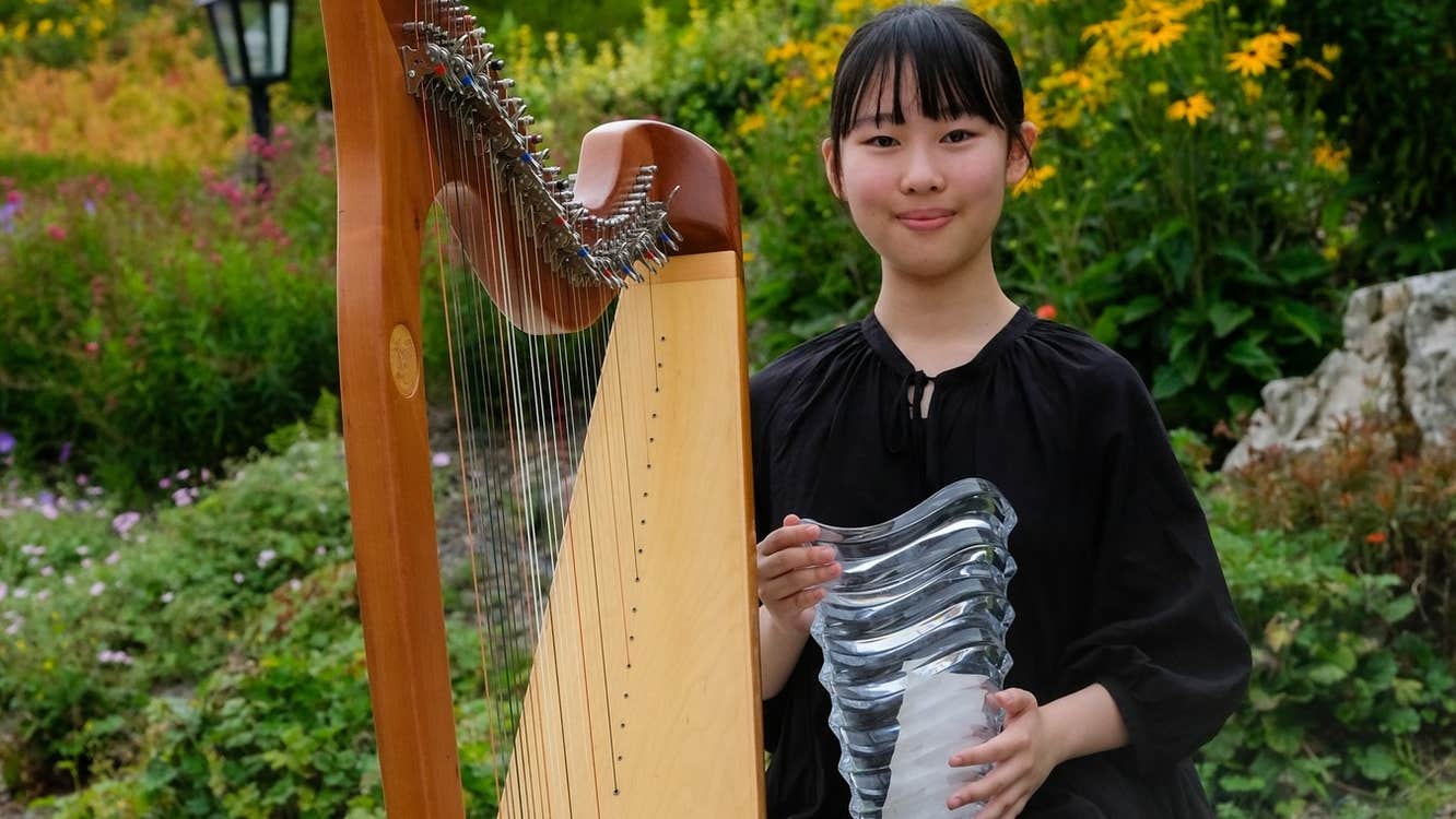 Winner of our International Harp Competition 2025, a smiling woman holding a glass trophy beside a harp.