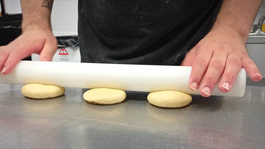 A person rolling three small slabs of dough with a rolling pin