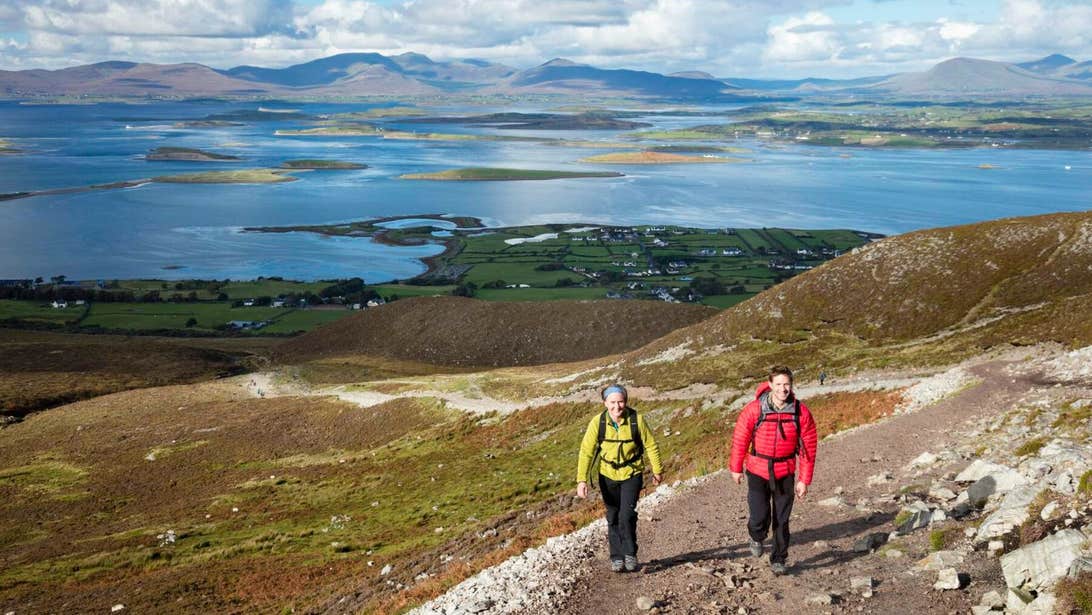 Two walkers on their way up Croagh Patrick in hiking gear with backpacks strapped across them.