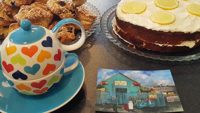 Colourful teapot cake and plate of scones on a table with photo of Kerry Creamery