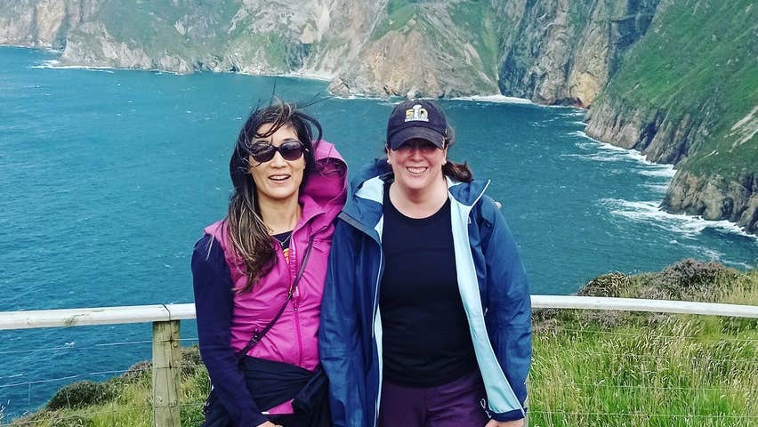Two ladies standing on a platform with the sea and cliffs behind them