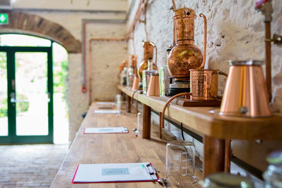 A wooden bench table, inside the Listoke Distillery and Gin School, which has copper distilling materials and machines on top.
