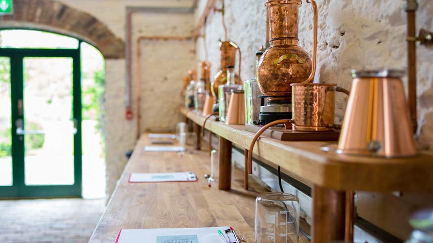 A wooden bench table, inside the Listoke Distillery and Gin School, which has copper distilling materials and machines on top.
