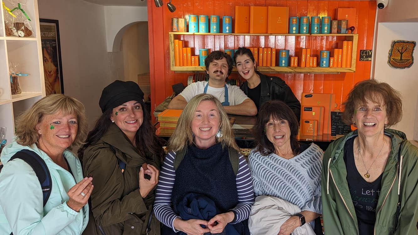 Group of people smiling for a picture with a shelf displaying chocolate and an orange wall in the background