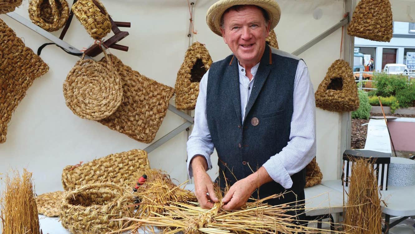 Image of Mr Padraig Larkin - a smiling man with items woven from straw on display.
