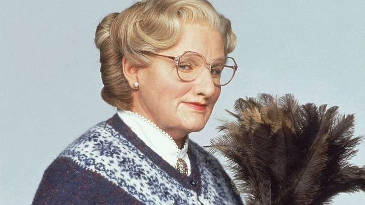 A older woman holding a feather duster looking slightly smug