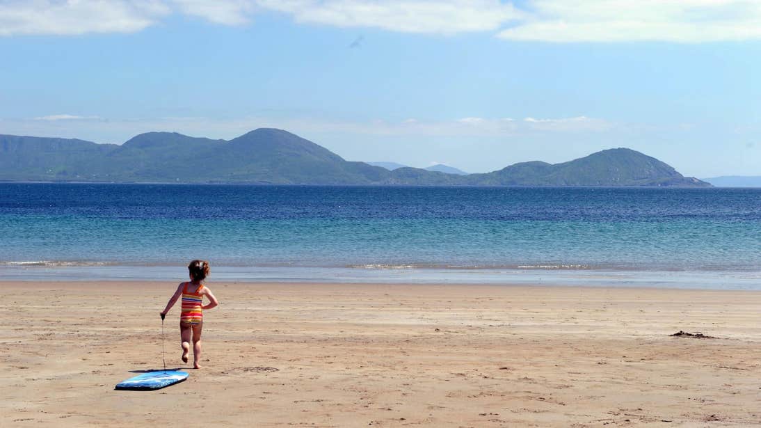 Little girl running on the sand towards the water at Ballinskelligs Beach in Kerry