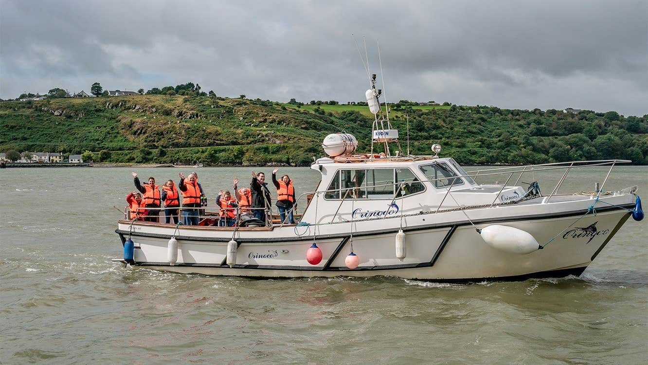 A group of people wearing orange life vests on a boat called the Orinoco