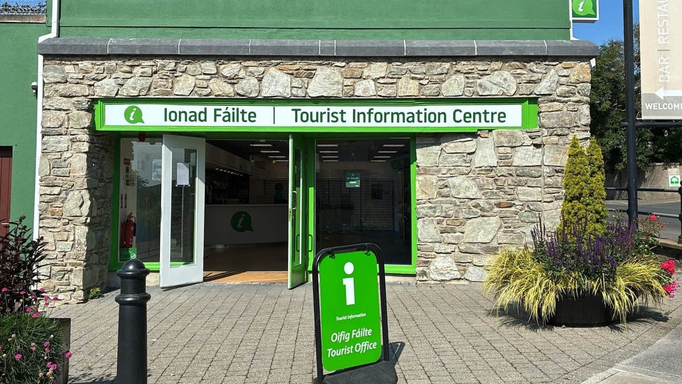 A stone clad shopfront with green and white signage for Clifden Tourist Information Centre
