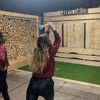 Two people one holding an axe in an axe throwing wooden area with targets in front