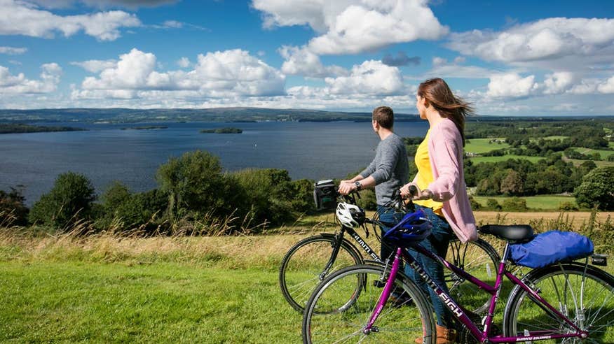 Two cyclists standing with their bikes looking out onto a lake