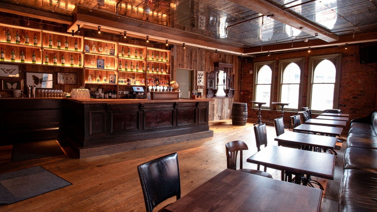 Interior of a pub with lots of wooden tables, flooring and bar along with old style windows