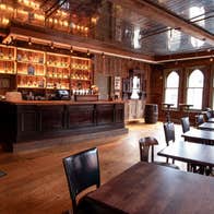 Interior of a pub with lots of wooden tables, flooring and bar along with old style windows