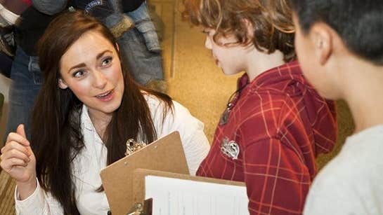 A woman with a clipboard is talking to 2 young children