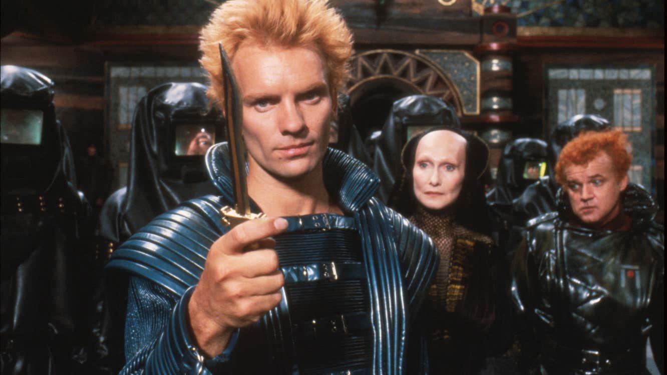 A man with a knife is standing in front of a group of people. They are wearing futuristic clothes.