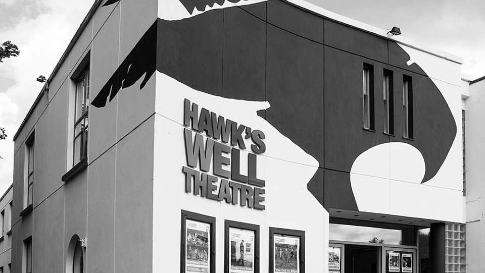 Black and white image of exterior of a theatre with three posters on the wall and railings to the left