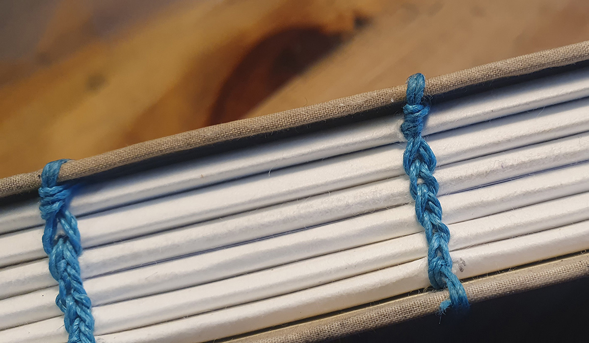 Coptic Stitch Bookbinding workshop with Blueway Art Studio. Close up view of hand stitching on a book with thick pages.