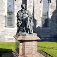 A large statue of a seated man on a plinth with church in the background.
