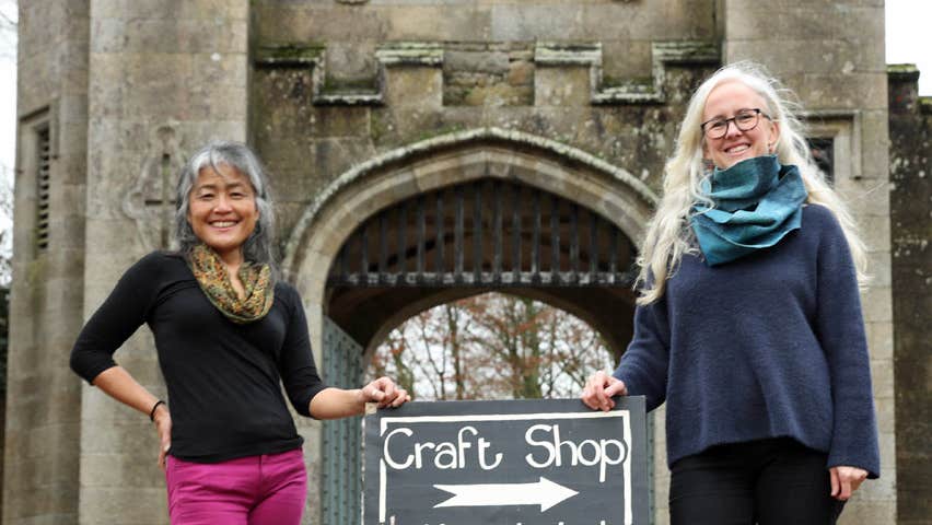 Two ladies standing outside a castle like gate lodge beside a sign that says crafts with an arrow pointing to the right