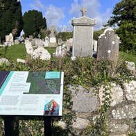 View over wall of a cemetery with a story board and old headstones
