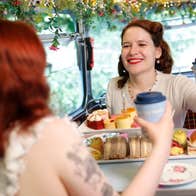 A woman seated at a table with mug and platter of sandwiches on top deck of double decker bus.