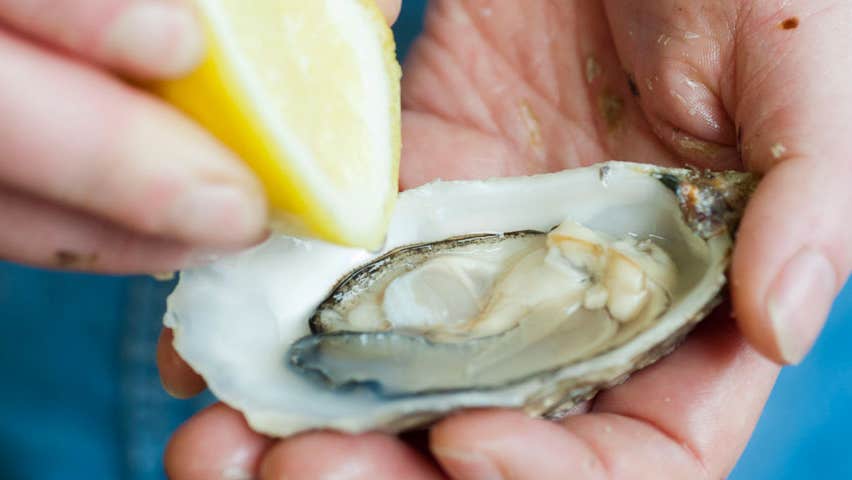 Freshly opened oyster being seasoned with lemon