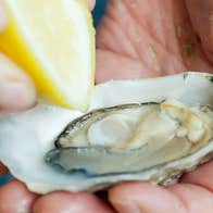 Freshly opened oyster being seasoned with lemon