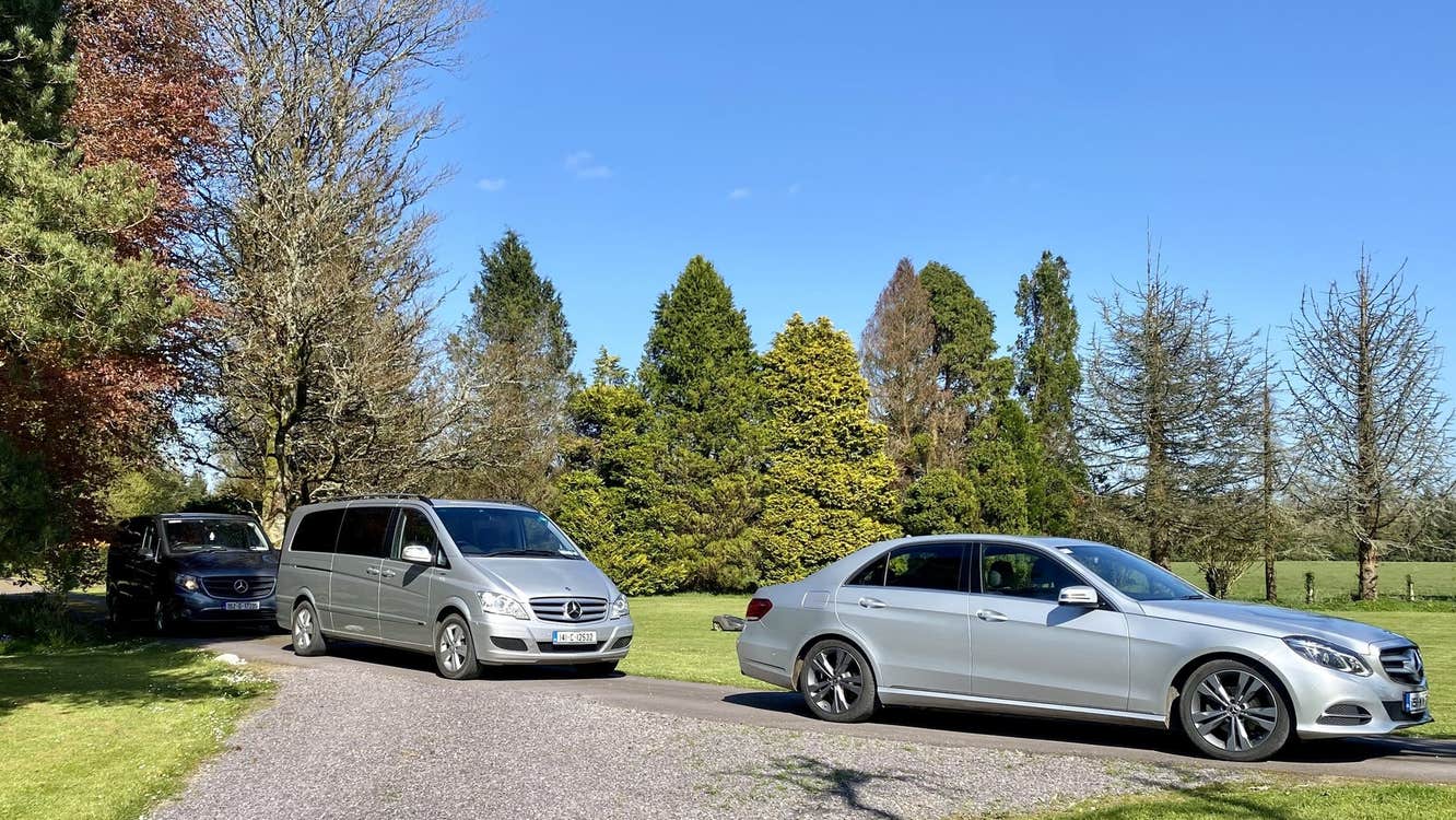 Three silver vehicles parked on a road in the middle of trees and a lawn