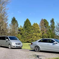 Three silver vehicles parked on a road in the middle of trees and a lawn