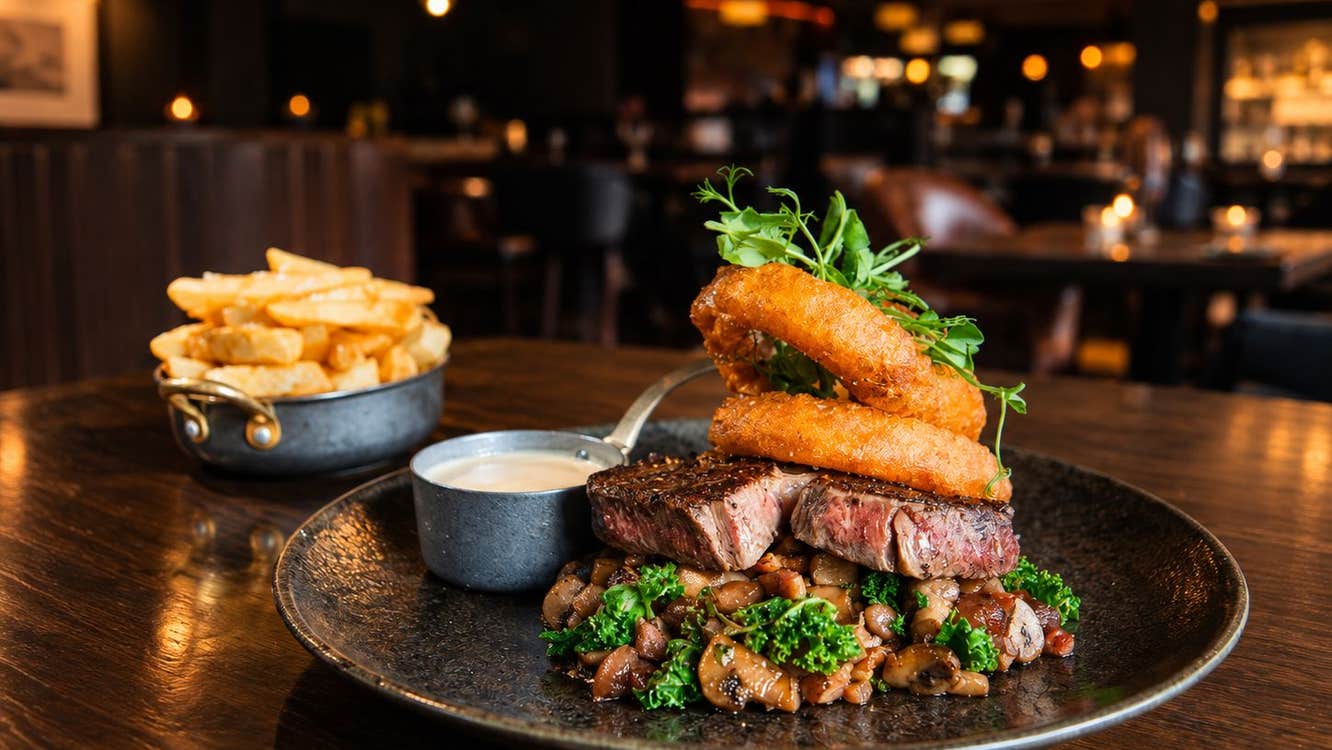 Steak with onion rings and a sauce on a plate with a portion of chips in the background
