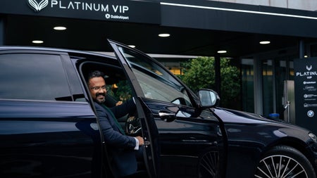 A person sits in the drivers seat of a car with the door open outside a building