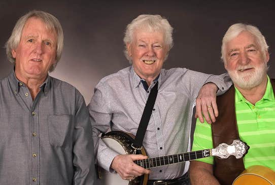 3 older men smiling with musical instruments.