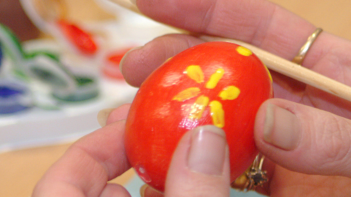 Close up shot of fingers holding an egg painted red with yellow motif on.
