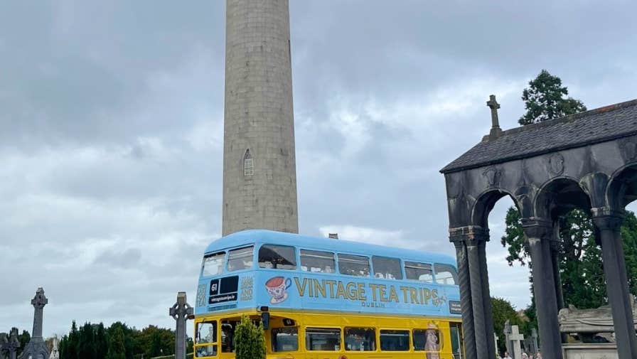 Vintage Tea Trips Bus at Glasnevin Cemetery, an old fashioned double decker bus park in a cemetery with tall thin round tower.
