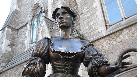 A statue of a woman in period dress on a city street