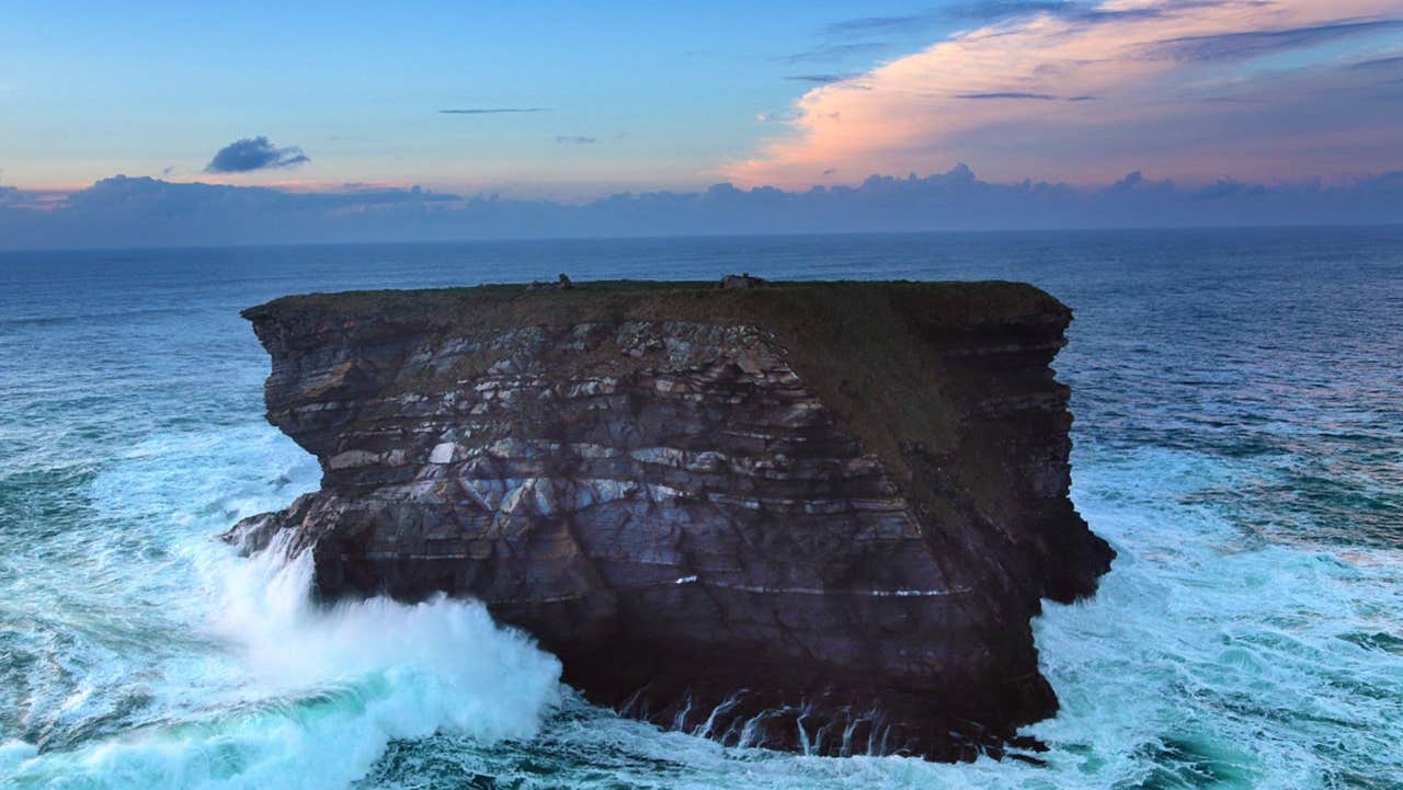 Waves crashing on a sea stack with the sun setting in the background