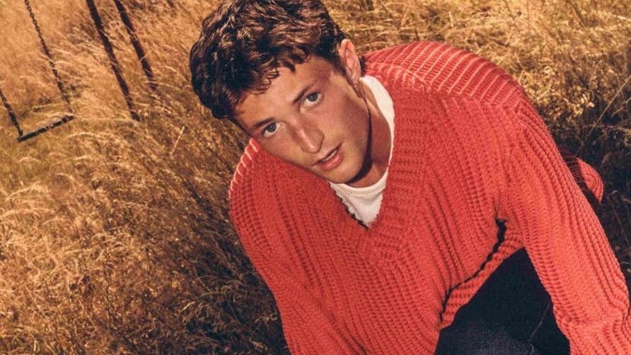 A young man in orange jumper in a field of brown long grass