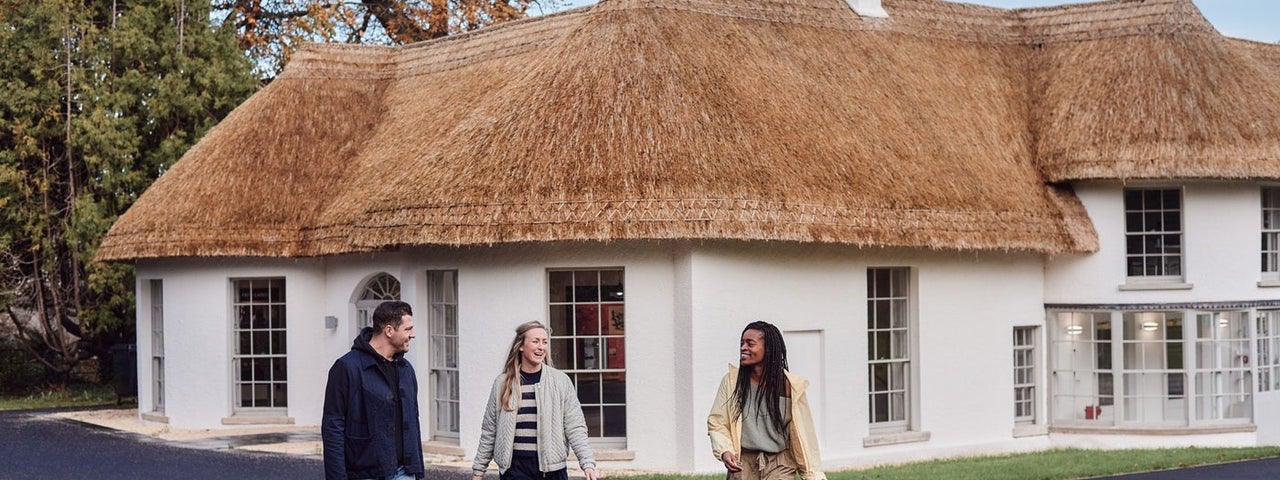 Three people walking away from a white building with a thatched roof
