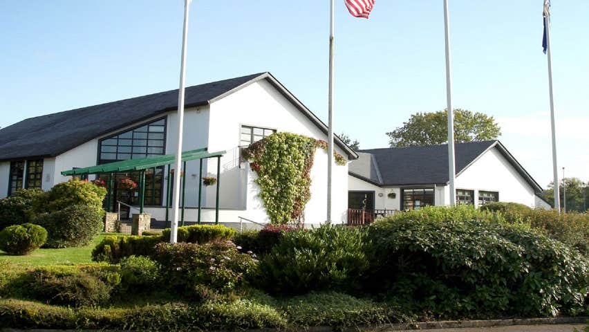 The exterior of Father Peyton Memorial Centre with shrubs and flag poles in front of building