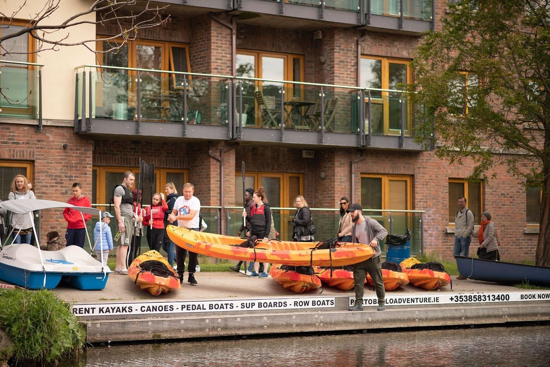 Group of people getting ready to take an orange kayak in to the water in front of an apartment block