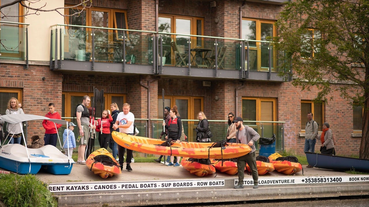 Group of people getting ready to take an orange kayak in to the water in front of an apartment block