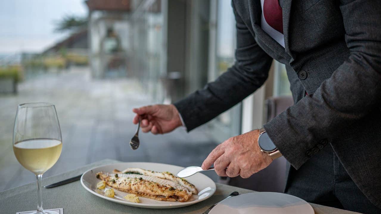 A fillet of grilled fish is being served with a glass of white wine