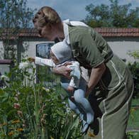 A woman is holding a baby close to a flower.