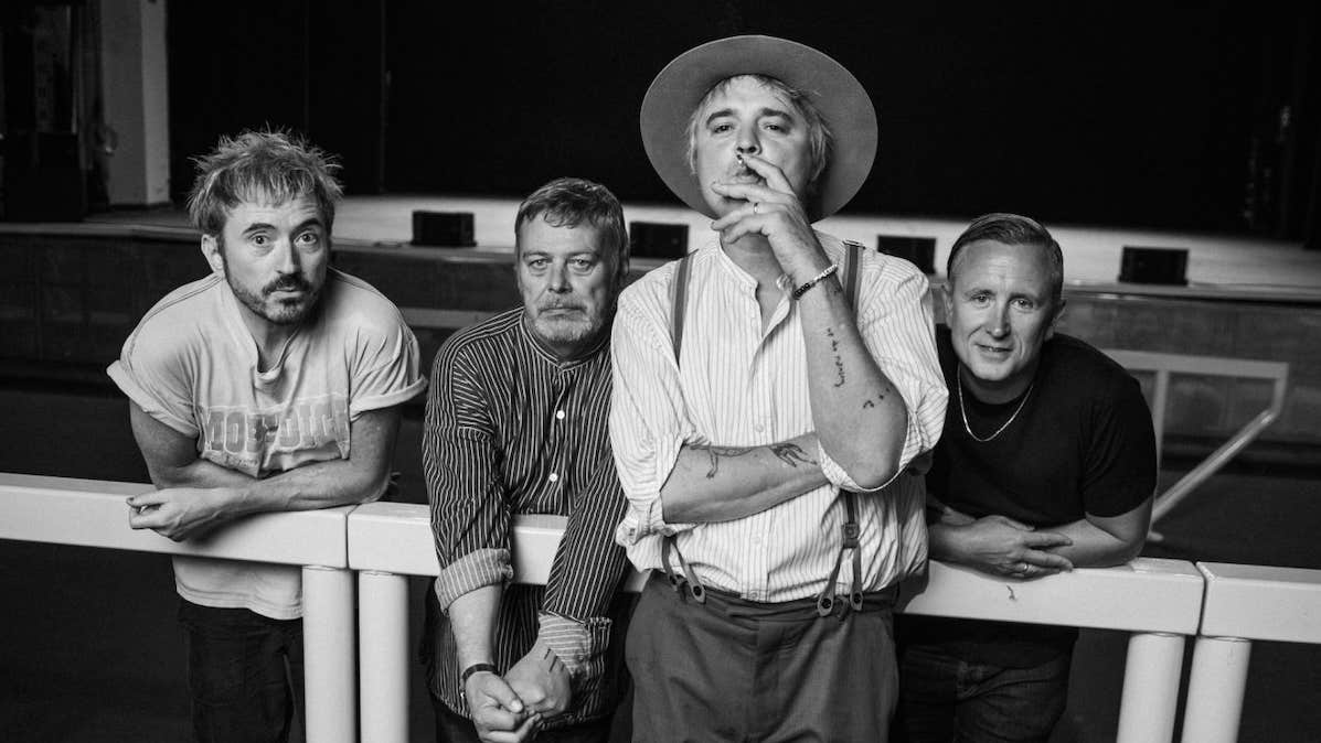 Black and white photo of 4 men leaning on or against a thick rail