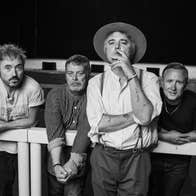 Black and white photo of 4 men leaning on or against a thick rail