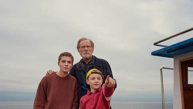 An older man with teenager and young boy pointing forward with sea in the background.