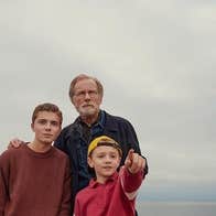 An older man with teenager and young boy pointing forward with sea in the background.