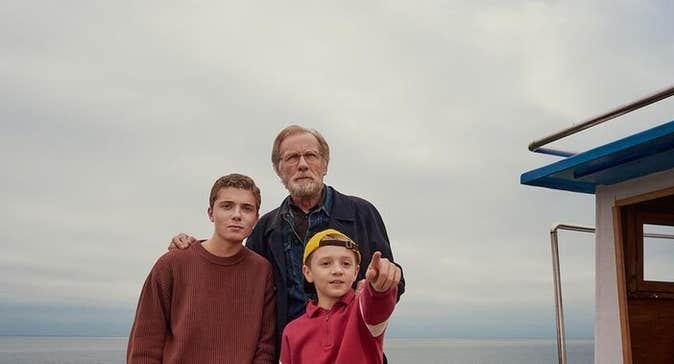 An older man with teenager and young boy pointing forward with sea in the background.