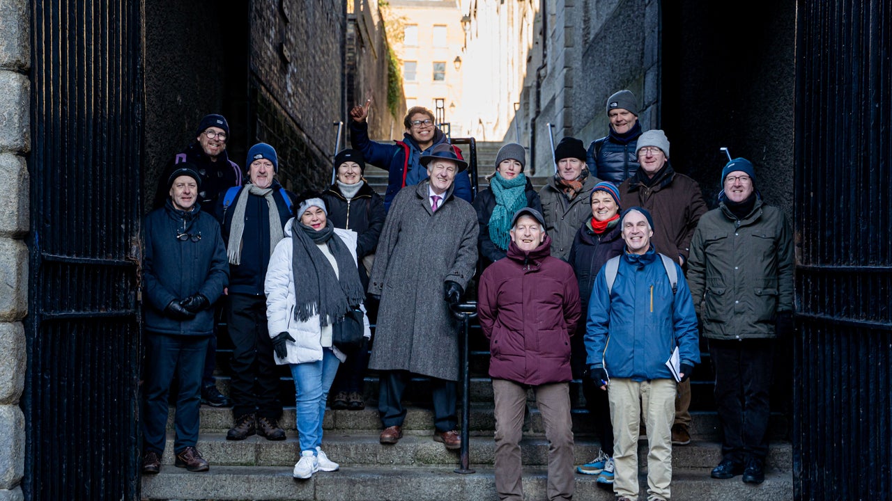 A guided walking tour group gathered on stone steps beneath an old iron gateway in Dublin, wrapped up against the cold as they explore the city's dark and storied past.